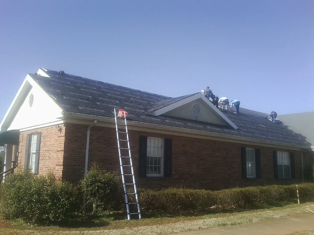 Crew tearing shingles off a brick ranch roof with a ladder set — Metal Roof Repair work by our crew in Centerville