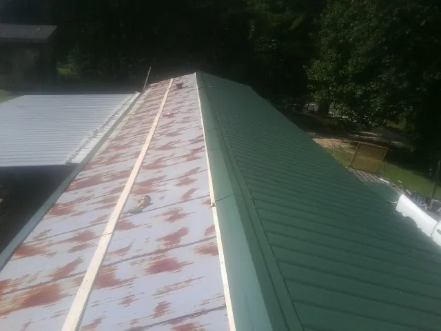 Old rusted panels beside newly installed green metal roofing — Wind Damage Roof Repair by Roofing Brothers in Centerville